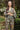 Woman wearing a floral patterned outfit standing outdoors with greenery in the background