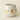 Speckled ceramic candle with gold circular designs on a beige background.