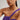 Woman wearing a purple dress and pearl necklace against a neutral background.