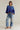 Woman wearing a blue knitted top and patchwork jeans on a plain background