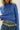 Person wearing a blue knitted sweater and jeans with a visible brand belt.