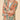 Model wearing a Floral Jungle Kimono Jacket in Petal, a lightweight, open-front jacket with a peach-toned base and a botanical print featuring green leaves and flowers. The model is smiling and crossing her arms, styled with a white top and neutral-colored pants against a soft beige background.