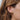 Close-up of a woman's ear adorned with two gold earrings: a small twisted knot stud and a sleek open hoop. The jewelry has a polished finish, complementing her warm brown hair.