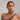 Woman wearing a purple top and pearl necklace against a plain background.