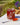 A jar of Saltspring Kitchen Co. Triple Pepper Jelly sits on a white table outdoors, with a spoonful of the red-orange jelly in the foreground and a blurred garden background.