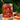A jar of Saltspring Kitchen Co. Triple Pepper Jelly sits on a white plate with slices of toast topped with the orange-red jelly, set against a blurred green garden background.