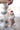 Small mouse ornament in a sleeping bag with a Santa hat, held by a hand against a blurred Christmas tree background.
