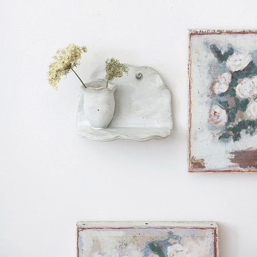 Stoneware vase wall shelf with fresh flowers mounted next to canvas artwork. 