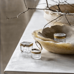 Set of 3 beveled glass and brass boxes styled on a marble table with branches. 