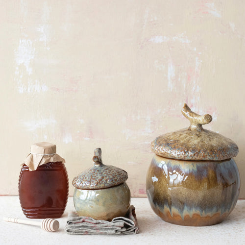 Stoneware acorn canisters on table with a jar of honey. 