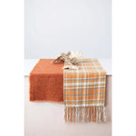 Burnt orange terracotta table runner on top of a table with a plaid blanket. 