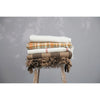 Plaid throw in a stack of blankets on top of a wooden stool. 