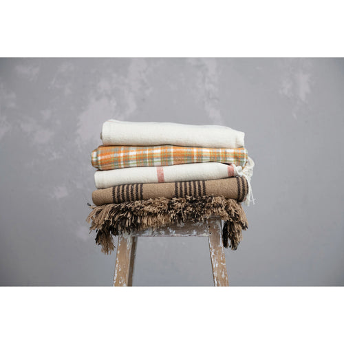 Plaid throw in a stack of blankets on top of a wooden stool. 