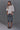 A woman modeling a white short-sleeve top with wide bell sleeves, paired with dark blue cropped denim jeans and black flat shoes, standing against a solid gray studio background.