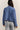 Person wearing a blue textured jacket and light gray jeans against a plain background