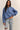Woman wearing a blue cropped sweater and light blue jeans against a plain background