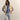 Person wearing a beige jacket, blue shirt, and ripped light blue jeans against a plain background