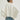 Person wearing a white jacket and blue jeans against a plain background