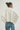 Person wearing a white jacket and blue jeans against a plain background