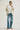Woman wearing a beige blazer, white shirt, and blue jeans on a plain background