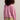 Person wearing a pink sweater and beige shorts against a plain background