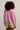 Person wearing a pink sweater and beige shorts against a plain background