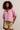 Woman wearing a pink sweater and beige shorts against a plain background
