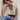 Woman wearing a white lace top and blue jeans against a plain background