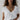 Woman wearing a white t-shirt with layered necklaces against a plain background