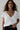 Woman wearing a white t-shirt with layered necklaces against a plain background