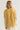 A woman shown from the back wearing a mustard yellow oversized top with floral patterned sleeves, photographed against a plain light gray studio background.