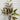 An artificial autumn leafy branch with green and brown leaves on a thin brown stem, displayed against a white painted brick wall background.