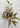 An artificial autumn leafy branch with green and brown leaves on a thin brown stem, displayed against a white painted brick wall background.