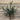 A single artificial olive branch with dark green leaves and stems, displayed against a rustic wooden plank background.
