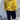 A person wearing a chunky knit mustard yellow mock neck sweater, dark navy cropped pants, and red pointed flats, standing against a white textured wall.