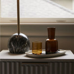 Amber glass carafe set out on a table underneath a window. 