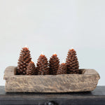 Small and large sized brown pinecone candles in a salvaged wooden bowl ontop of mantel. 