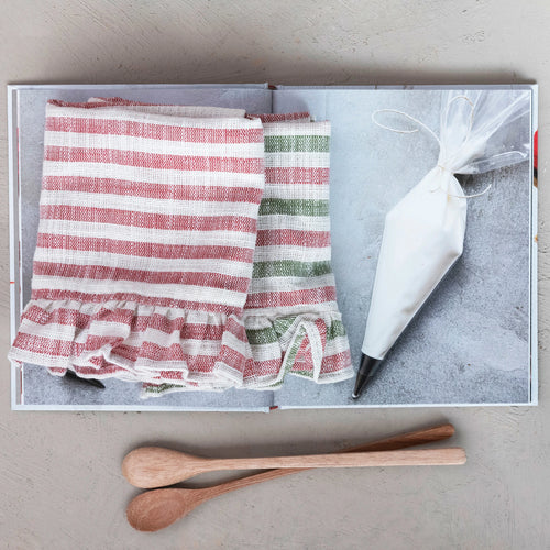 Set of two festive striped tea towels on a baking magazine with two wooden spoons.