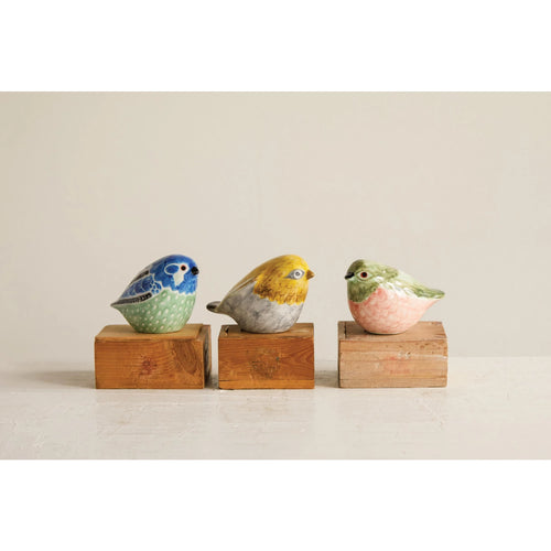 Three stoneware colorful birds sitting on wooden blocks.