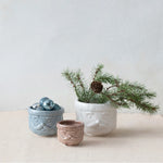 Three charming decorative stoneware santas, styled with ornaments and pine branches.