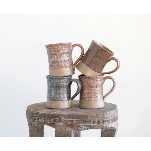 Four stoneware mugs with glaze placed on top of an antique table. 