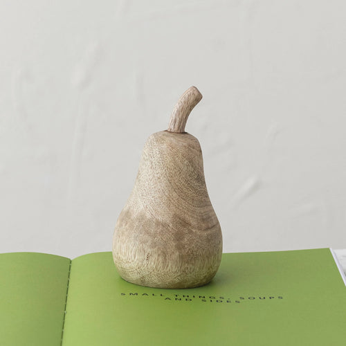 Hand carved mango wood pear resting on a cook book.