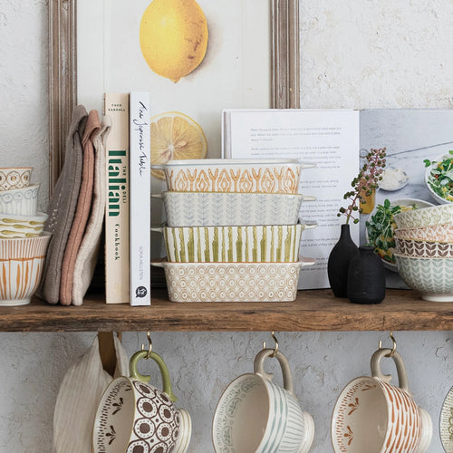 Various Stoneware bakers styled on a shelf with cookbooks, matching bowls and mugs. 