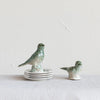 Two debossed stoneware birds perched on some matching decorative plates. 