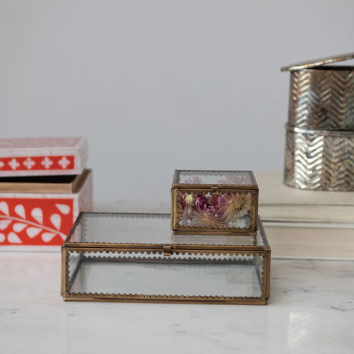 Brass and glass display box with smaller version placed on top holding some dried florals.