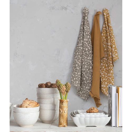 Cotton printed and waffle tea towels in two different colors, hanging from a hook on the wall styled with stoneware dishes.