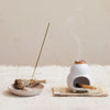 Stoneware incense holder holding an incense stick beside a different style incense holder.