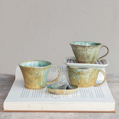 Three stoneware glazed mugs resting on an open book.