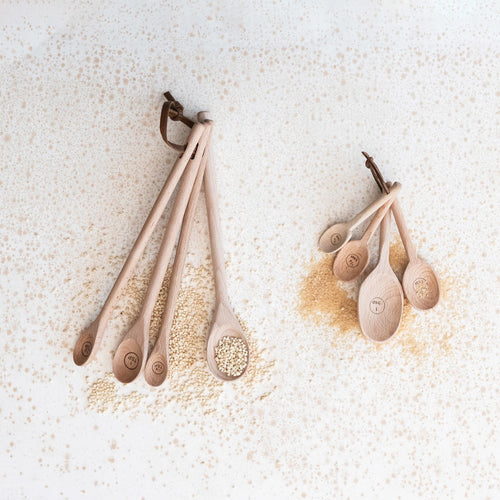 Four carved beech wood measuring spoons styled with some powdered spices. 