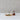 Wooden snail-shaped appetizer pick holder with four stainless steel picks, each topped with a wooden handle. One pick is placed in olives and cheese on parchment paper, while the snail holds the rest. The minimalist backdrop highlights the natural wood tones and functional design.